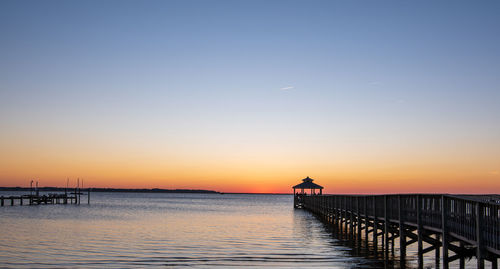 Silhouette pier on sea against clear sky during sunset