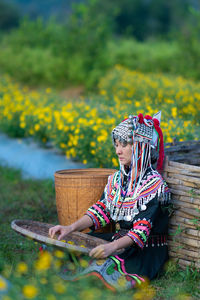 Woman in traditional clothing holding straw basket sitting at farm