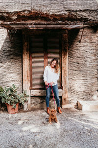 Full length of woman with dog standing against wall