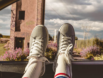 Low section of person relaxing by plants against sky