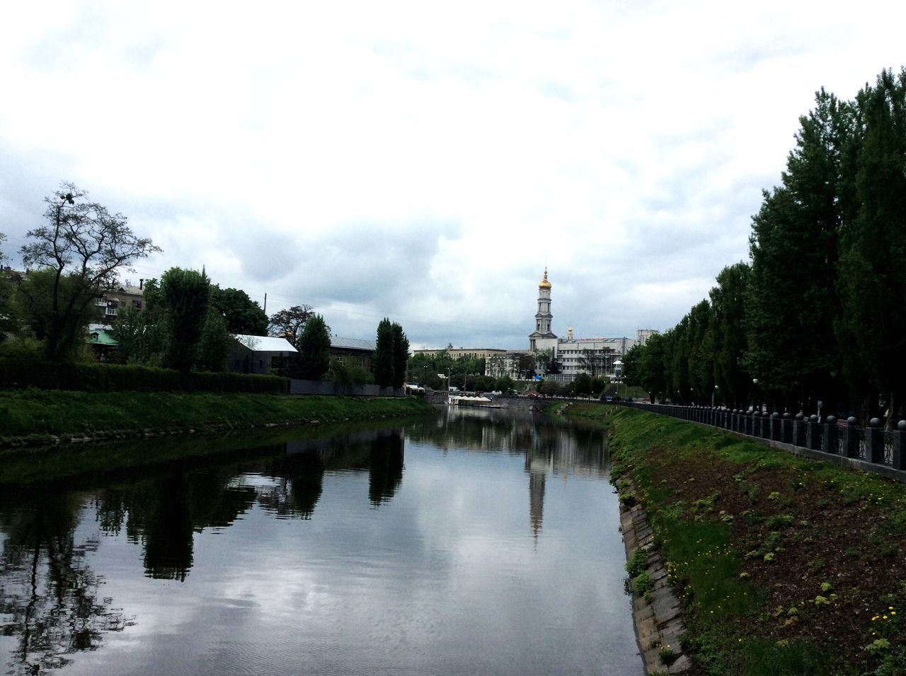 tree, sky, water, reflection, built structure, architecture, cloud - sky, building exterior, waterfront, growth, green color, tranquility, river, nature, cloud, canal, day, pond, tranquil scene, outdoors