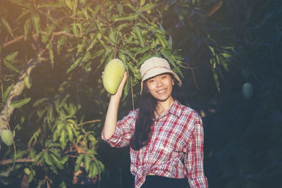 Portrait of female farmer holding mangoes in farm