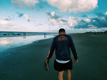 Rear view of man standing on beach against sky