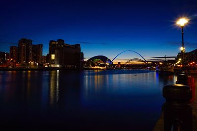 Illuminated buildings by river against sky at night