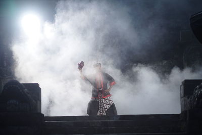 Man holding smoke stack against built structure