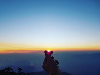 Optical illusion of person hand holding sun against sky during sunset