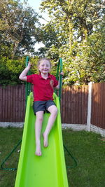 Full length of smiling girl sitting on plant against trees