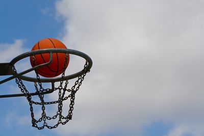 Low angle view of basketball in mid-air amidst hoop against sky