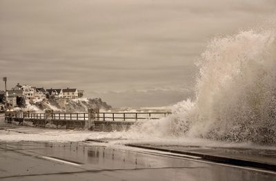 Wave splashing on retaining wall of promenade against sky