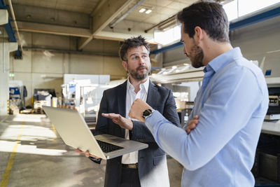 Businessmen working on laptop while standing at factory