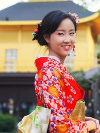 Portrait of smiling young woman in traditional clothing standing against house