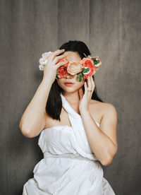 Young woman with flowers in front of face against wall