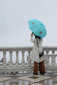 Woman with umbrella standing by railing against sky during rainy season