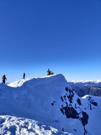 People on snowcapped mountain against blue sky