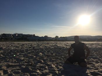 Portrait of man sitting on beach against sky during sunset