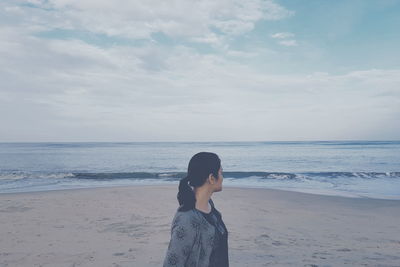 Woman standing at beach against cloudy sky