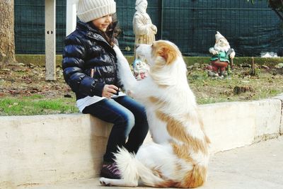 Girl wearing warm clothing sitting with dog against statues at park