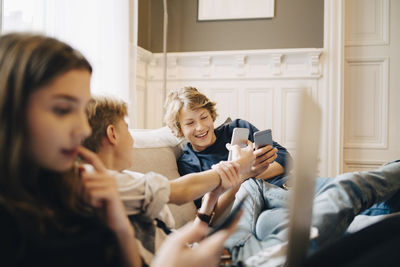 Boys using mobile phone while sitting with female friend on sofa