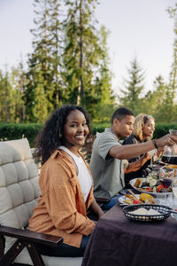 Portrait of smiling woman sitting with male and female friends while having food at dinner party in back yard