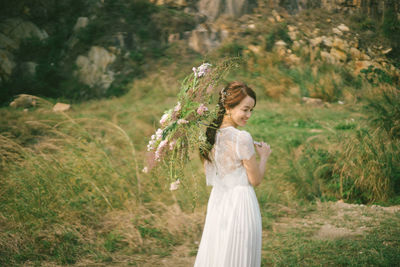 Side view of bride holding umbrella while standing on grassy field