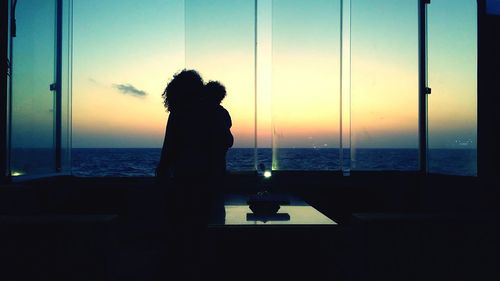 Silhouette of woman looking at sea through window