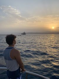 Rear view of man looking at sea against sky during sunset