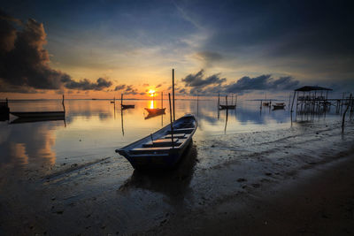 Boat moored on shore against sky during sunset