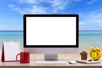 Computer with office supplies on desk against beach