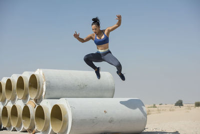 Woman jumping over pipe against sky