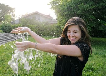 Water splashing on happy woman standing at grassy field