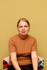Portrait of young woman sitting against yellow background