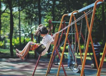 Side view of girl playing on swing at playground