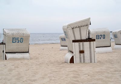 Hooded chairs on sand at beach against sky