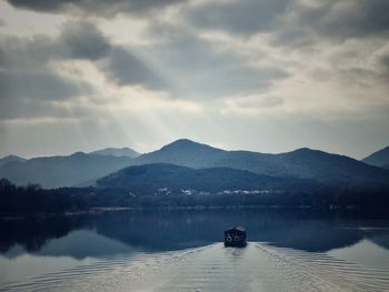 Boat sailing on lake by mountains against sky