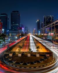 Illuminated railroad tracks amidst buildings in city against sky at night