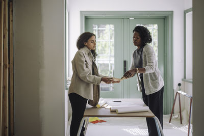 Female client comparing building material while talking with architect at under construction apartment