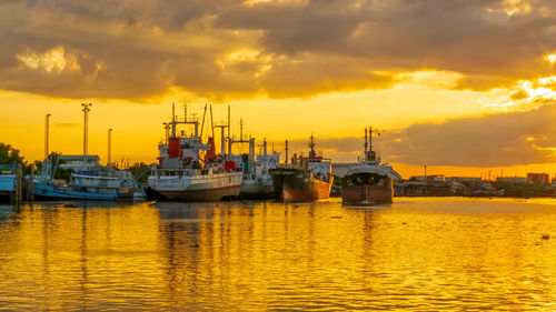 Boats moored at harbor against sky during sunset