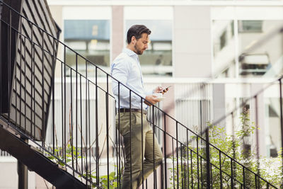 Side view of businessman using smart phone while moving down steps of log cabin
