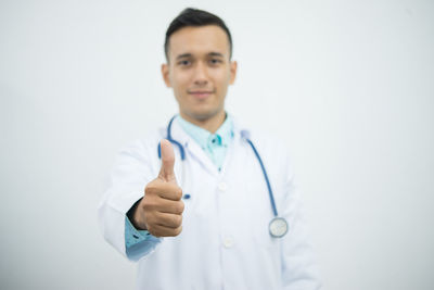 Midsection of doctor showing thumbs up over white background