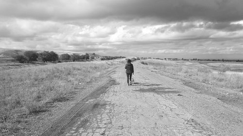 Rear view of man walking on landscape against sky