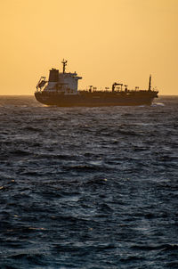 Silhouette ship sailing on sea against clear sky during sunset