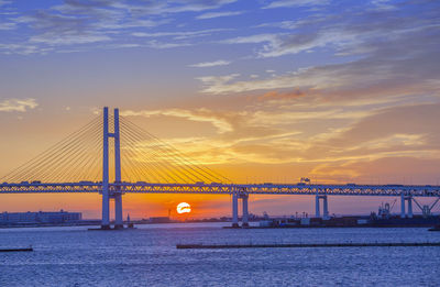 Cable-stayed bridge over sea against orange sky during sunset