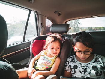 Siblings looking at digital tablet while sitting in car