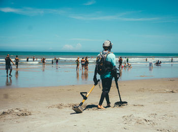 Person with equipment walking at beach against blue sky