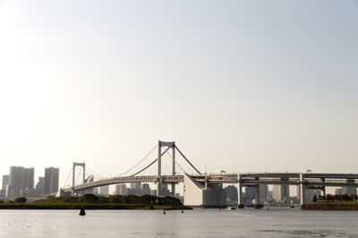 Rainbow bridge over tokyo bay in city against clear sky