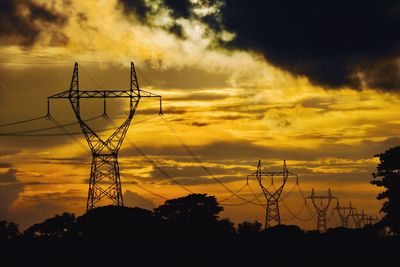 Low angle view of silhouette electricity pylon against dramatic sky