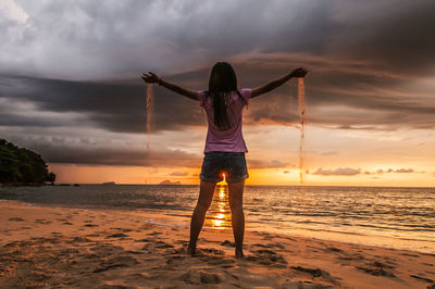 Rear view of man standing on beach against cloudy sky