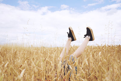 Low section of woman with legs-up amidst cereal plants on field