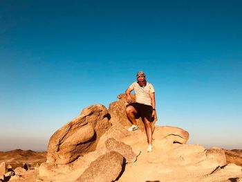 Man standing on rock against blue sky