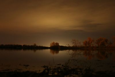 Reflection of silhouette trees in lake against sky at sunset